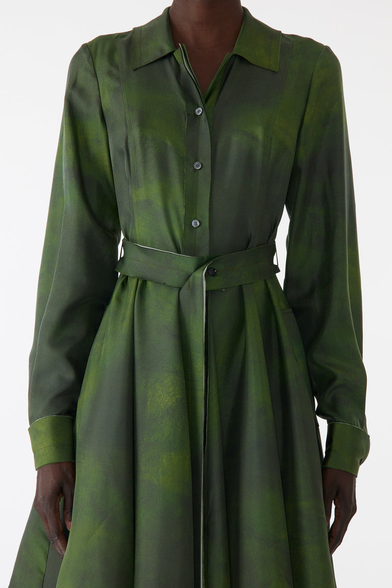 Model wearing a green silk twill shirtdress with long sleeves, asymmetric skirt, matching belt, and white-edged hem. view 4