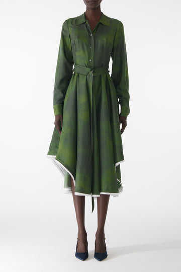 Model wearing a green silk twill shirtdress with long sleeves, asymmetric skirt, matching belt, and white-edged hem. view 1