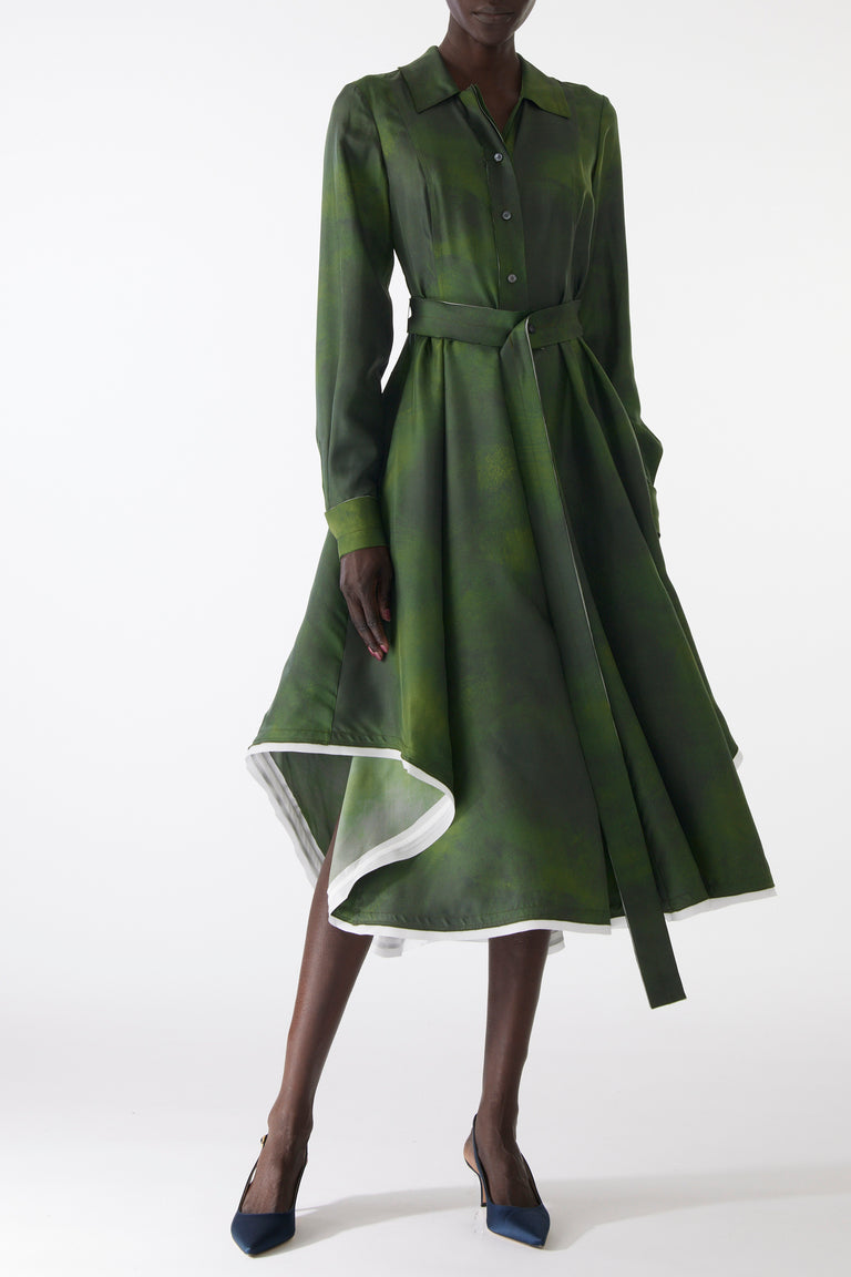Model wearing a green silk twill shirtdress with long sleeves, asymmetric skirt, matching belt, and white-edged hem. view 2