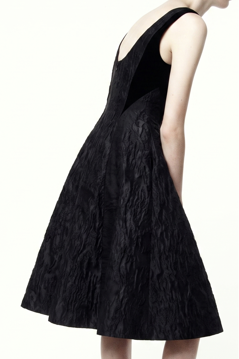 A sleeveless black dress with a textured crinkled fabric, shown from a side-back angle on a model against a plain white background. view 1