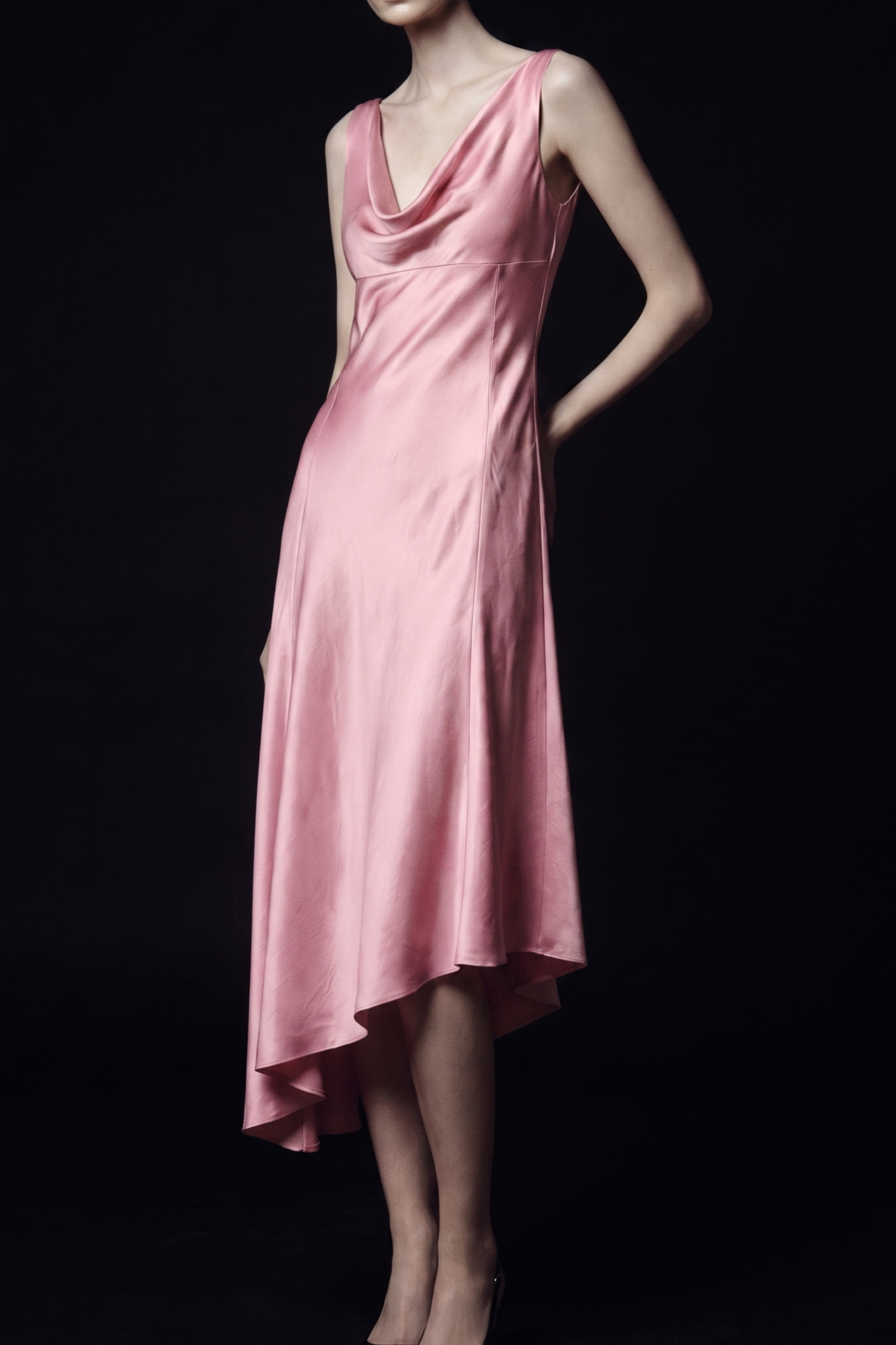 A woman modeling a sleeveless, high-neck satin midi dress in a soft pink color, set against a solid black background. view 1