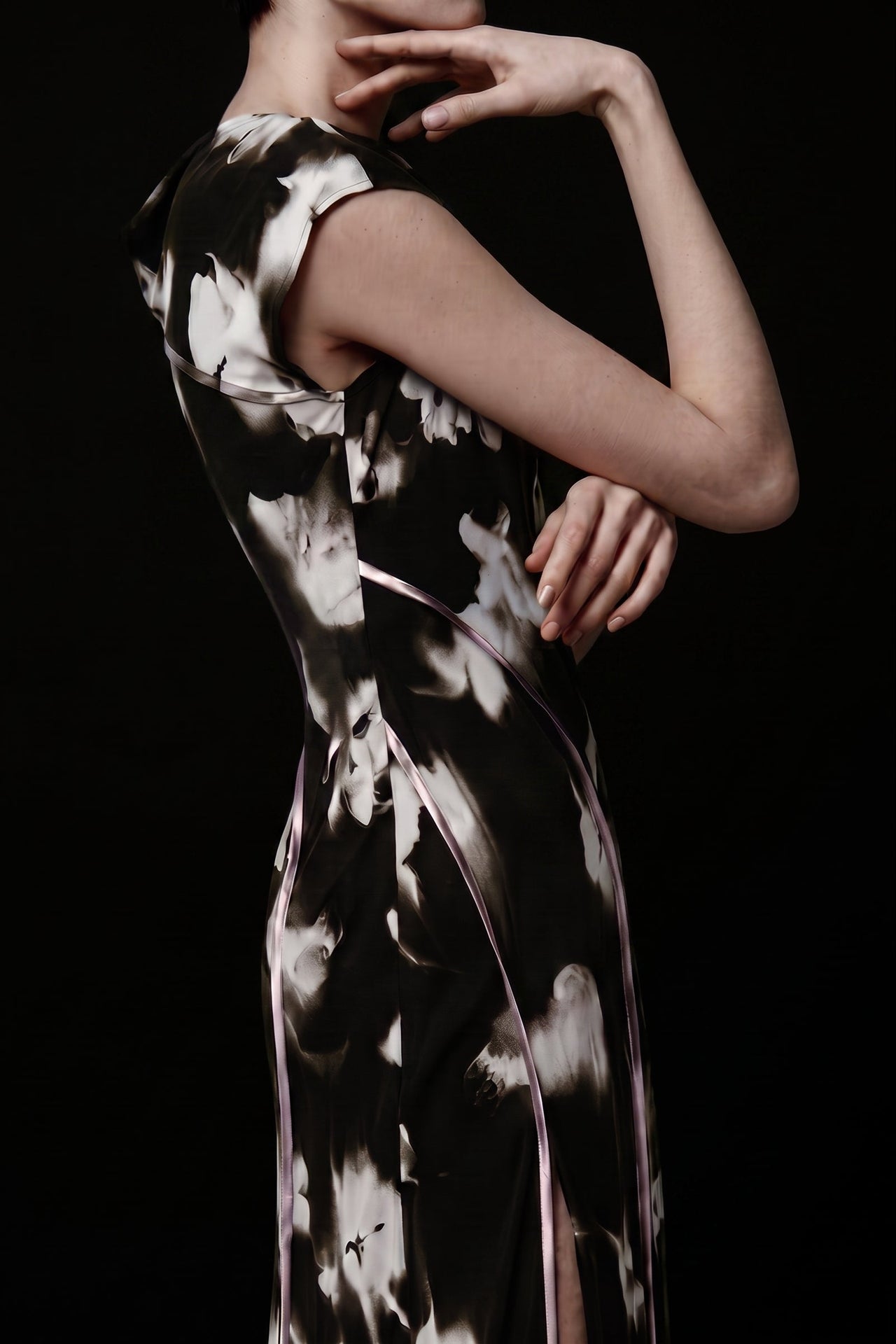 A model wearing a sleeveless black and white abstract patterned dress, shown from a side-back angle against a solid black background. view 1