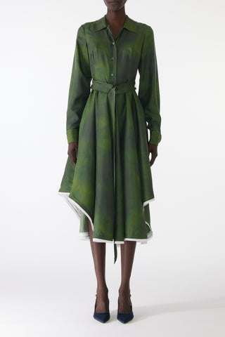 Model wearing a green silk twill shirtdress with long sleeves, asymmetric skirt, matching belt, and white-edged hem.