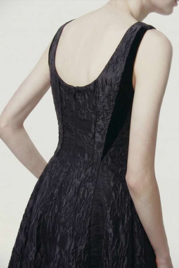 A woman shown from the back wearing a sleeveless black textured dress against a plain light background. view 2