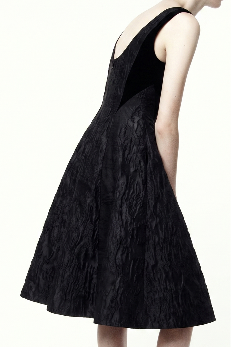 A sleeveless black dress with a textured crinkled fabric, shown from a side-back angle on a model against a plain white background. view 1