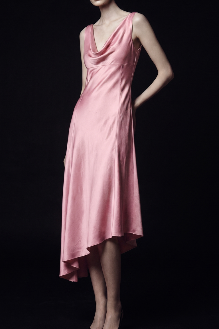 A woman modeling a sleeveless, high-neck satin midi dress in a soft pink color, set against a solid black background. view 1